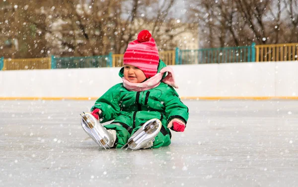 Милая маленькая девочка сидит на льду с коньками — стоковое фото