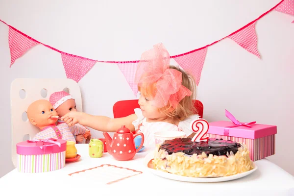 Glad söt liten flicka med sötsaker och dockor på födelsedag — Stockfoto