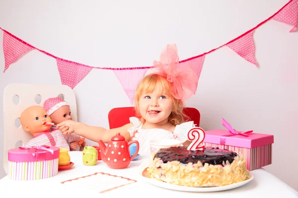 Glad söt liten flicka med sötsaker och dockor på födelsedag — Stockfoto