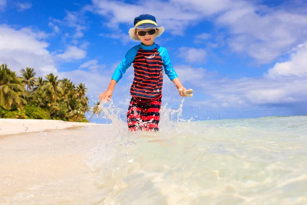 Kleine jongen stromend spatten water op strand — Stockfoto