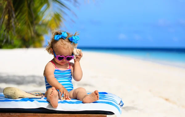 Cute dziewczynka słuchając powłoki na plaży — Zdjęcie stockowe