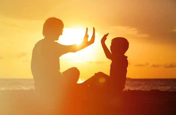 Vader en zoon spelen op zonsondergang zee — Stockfoto