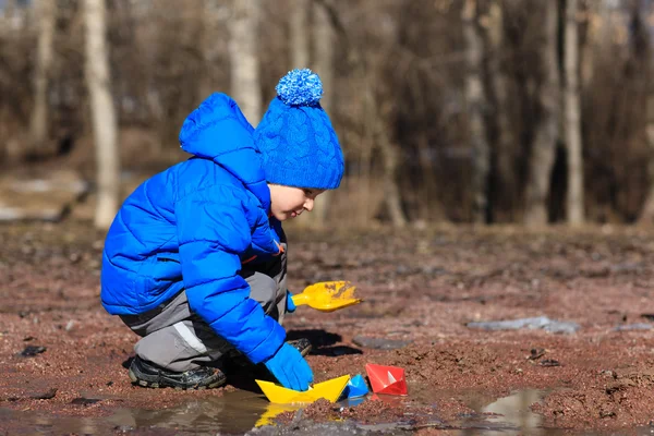 Little boy plaing with paper boats in spring puddle — Stock Photo, Image