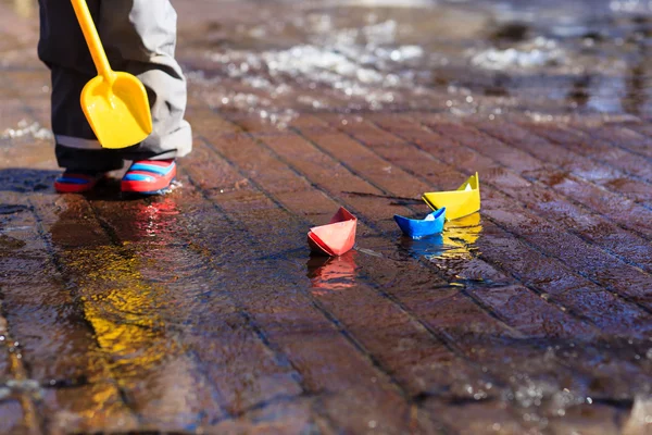 Niño jugando con barcos de papel en charco de primavera — Foto de Stock