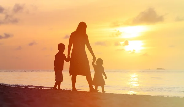 Mutter und zwei Kinder spazieren bei Sonnenuntergang am Strand — Stockfoto