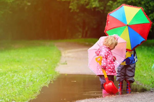 Küçük erkek ve kız su birikintisine oynarken şemsiye ile — Stok fotoğraf