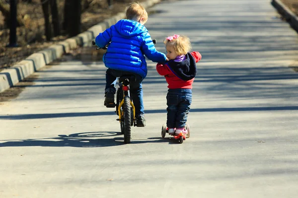 Kleiner Junge auf dem Fahrrad bringt kleinen Mädchen Rollerfahren bei — Stockfoto