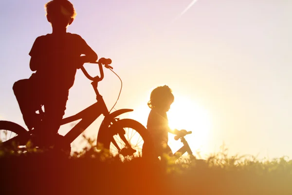 Menino e menina andando de bicicleta ao pôr do sol — Fotografia de Stock