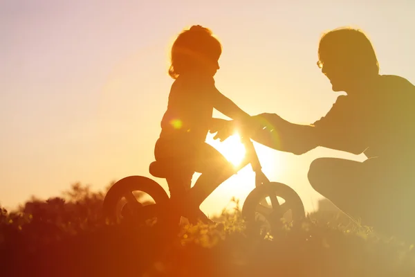 Pai ensinando filha a andar de bicicleta ao pôr do sol — Fotografia de Stock