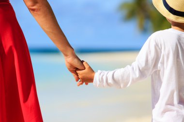 Anne ve oğlu kumsalda el ele tutuşuyorlar.