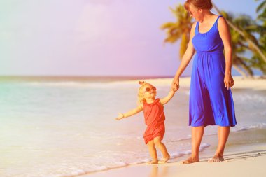 Anne ve küçük kızı tropikal plajda yürüyor.