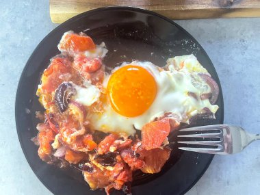 Siyah tabakta domates ve soğanlı sahanda yumurta, sağlıklı kahvaltı veya brunch konsepti. Yüksek kalite fotoğraf