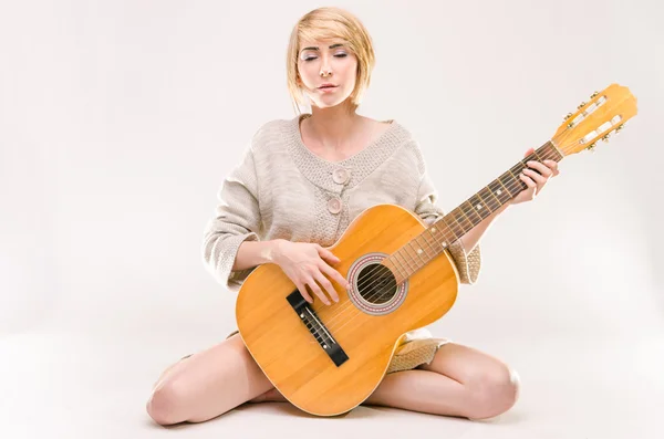 Young beautiful smiling blonde lady in gray sweater playing acoustic guitar — Stock Photo, Image