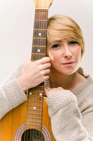 Young beautiful smiling blonde lady in gray sweater playing acoustic guitar — Stock Photo, Image