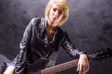 Elektro gitar siyah bir zemin üzerine siyah deri ceket giymiş güzel genç sarışın