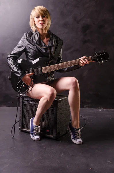 Beautiful young blonde dressed in black leather jacket with electric guitar on a black background — Stock Photo, Image