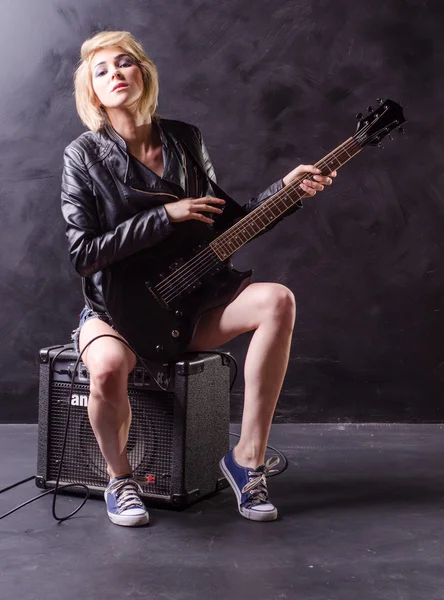 Linda jovem loira vestida com jaqueta de couro preto com guitarra elétrica em um fundo preto — Fotografia de Stock