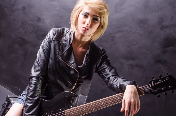 Beautiful young blonde dressed in black leather jacket with electric guitar on a black background — Stock Photo, Image