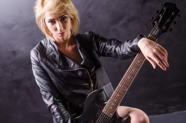 Красива молода блондинка, одягнена в чорну шкіряну куртку з електрогітарою на чорному тлі Ліцензійні Стокові Фото