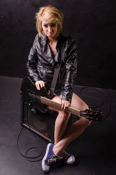 Beautiful young blonde dressed in black leather jacket with electric guitar on a black background — Stock Photo, Image