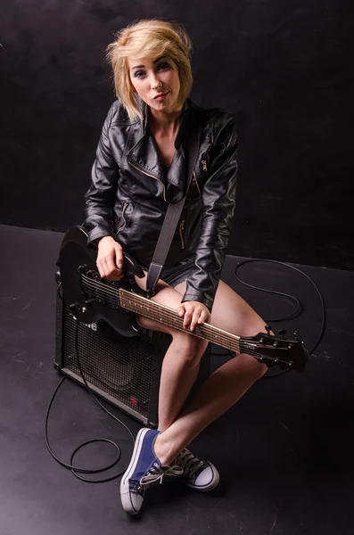 Beautiful young blonde dressed in black leather jacket with electric guitar on a black background — Stock Photo, Image