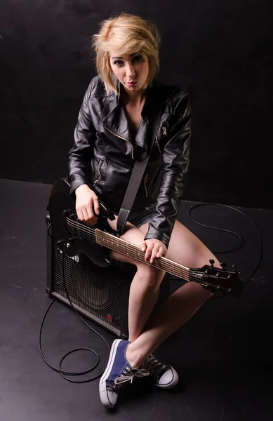 Beautiful young blonde dressed in black leather jacket with electric guitar on a black background — Stock Photo, Image