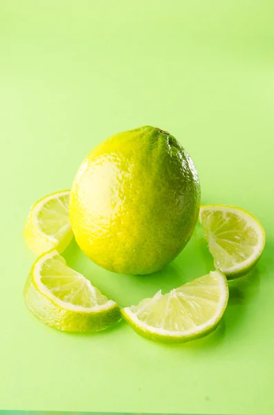 Slice of lime around one whole on green background, vertical shot — Stock Photo, Image