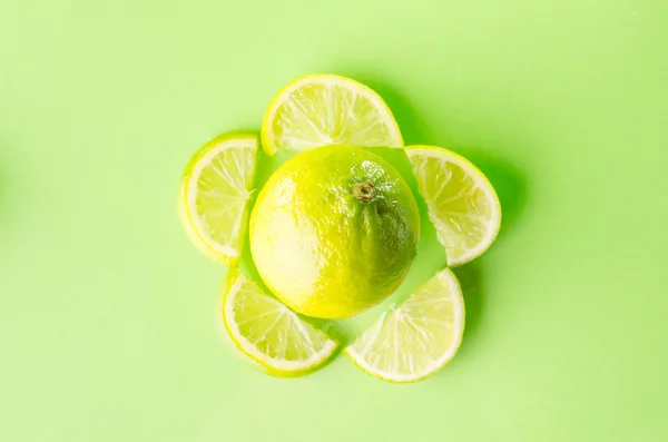 Slice of lime around one whole on green background, horizontal shot — Stock Photo, Image