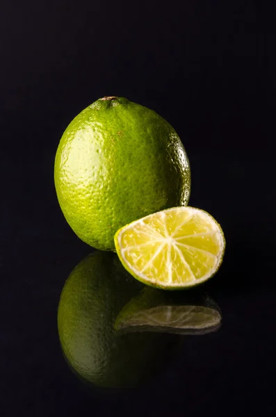 Um limão inteiro com fatia cortada no fundo preto, tiro vertical — Fotografia de Stock