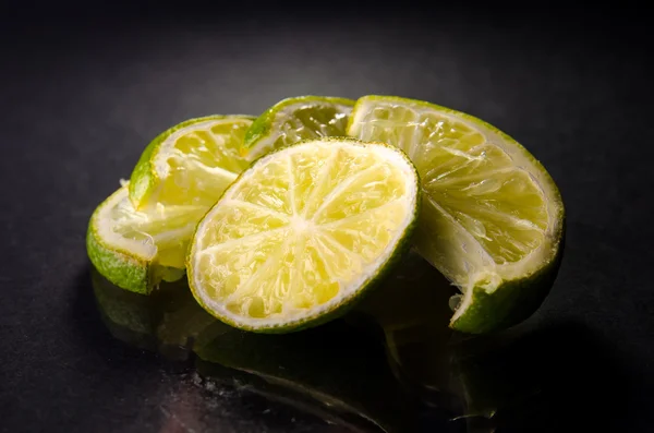 Green sliced limes with water drops on black background, horizontal shot — Stock Photo, Image