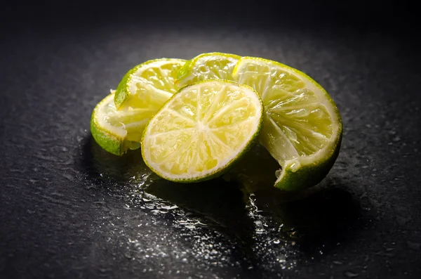 Green sliced limes with water drops on black background, horizontal shot — Stock Photo, Image