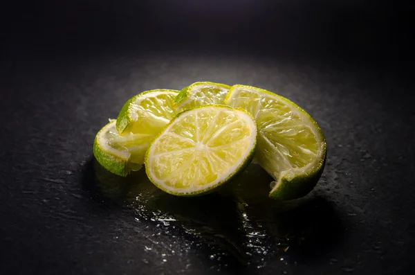 Green sliced limes with water drops on black background, horizontal shot — Stock Photo, Image