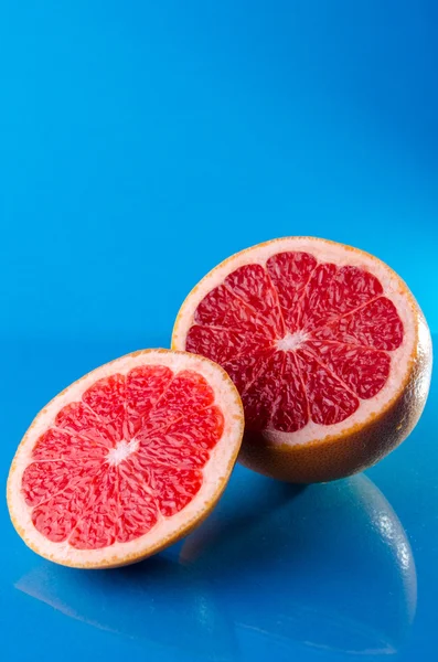 Inteiro e cortado em metade de toranja em um fundo azul, tiro vertical — Fotografia de Stock