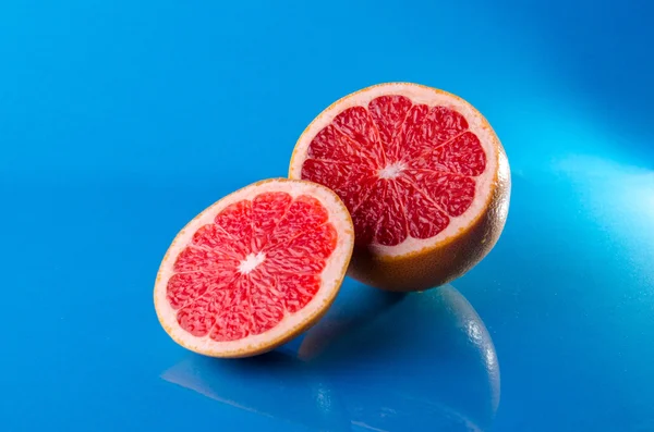 Inteiro e cortado em metade de toranja em um fundo azul, tiro horizontal — Fotografia de Stock