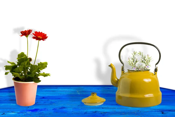 デザインのための空白のスペースを持つ地中海の青い木製のテーブルの鍋にローズマリーと赤のデイジーのガーベラの花の小枝と黄色のティーポット — ストック写真