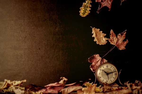 Old clock and autumn leaves background — Stock Photo, Image