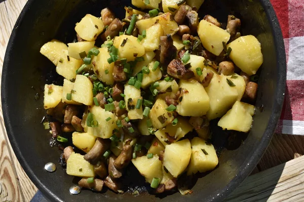 Close-up of fried potatoes with mushrooms and green onions, top view