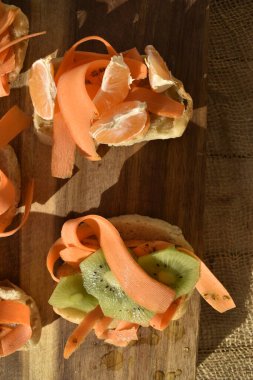 Kivili, portakallı ve tahta üzerinde havuç dilimli meyveli sandviç.