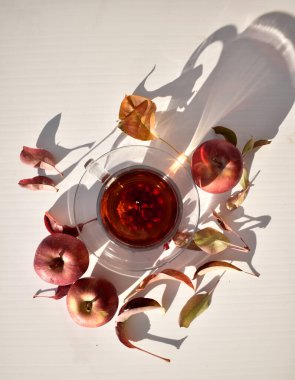 Beyaz zemin üzerinde kırmızı elmalar ve yapraklar olan şeffaf bardakta kış çayı, üst görünüm, boşluk kopyala