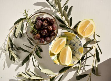 Baharatlı, limon dilimleri ve beyaz arka planda zeytin yapraklarıyla marine edilmiş siyah zeytinli kase.