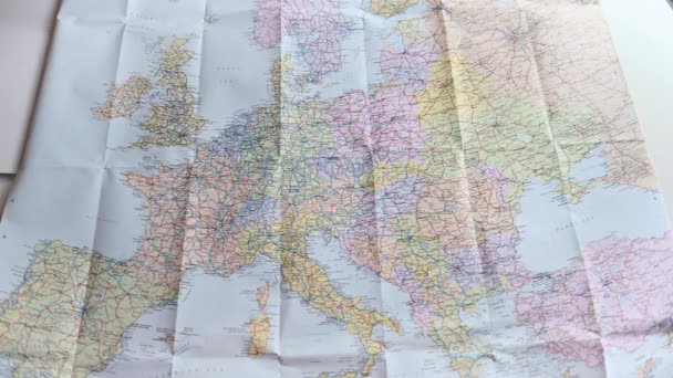 Cestovní pasy a různé měny v plastovém sáčku jsou házeny na barevnou mapu Evropy. Většina Evropy je v rámu. Krátký klip pro ilustraci cestování a cestovního ruchu. Real time 4K stock záběry od Brian Holm Nielsen