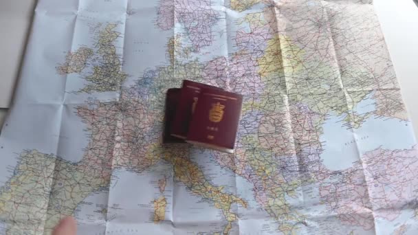 Cestovní pasy a různé měny v plastovém sáčku jsou házeny na barevnou mapu Evropy. Většina Evropy je v rámu. Krátký klip pro ilustraci cestování a cestovního ruchu. Zpomalený pohyb 1080p stock záběry Brian Holm Nielsen
