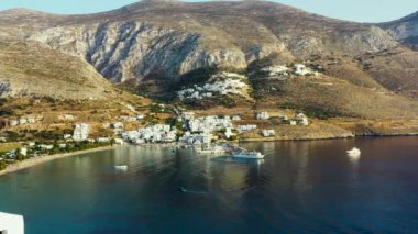 Aegialis 'in Yunanistan' daki İHA videosu. İnsansız hava aracı dağlarla çevrili küçük bir kasabanın ve berrak mavi suyun üzerinde uçar. Küçük bir marina ve limana doğru giden bir tekne var..