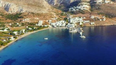 Aegialis 'in Yunanistan' daki İHA videosu. İnsansız hava aracı dağlarla çevrili küçük bir kasabanın ve berrak mavi suyun üzerinde uçar. Küçük bir marina ve limana doğru giden bir tekne var..