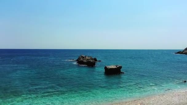 ドローンはギリシャのダモハリの岩のビーチを飛んでいます 透き通った青い海の上で続きます 雲のない美しい晴れた日です 1080P — ストック動画