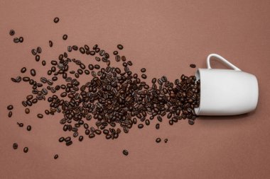 Renkli bir arka plana yayılmış kavrulmuş kahve çekirdekleri. Fasulyeler beyaz bir fincandan yayılmış..