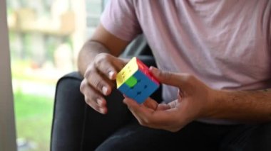 Kendi evinde rahat bir sandalyede oturan genç adam Rubiks küpünün 3 boyutlu bulmacasını çözüyor. Yüzün görünmez, sadece küpe odaklan. Kısa klip