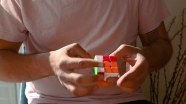 Kendi evinde rahat bir sandalyede oturan genç adam Rubiks küpünün 3 boyutlu bulmacasını çözüyor. Yüzün görünmez, sadece küpe odaklan. Kısa klip