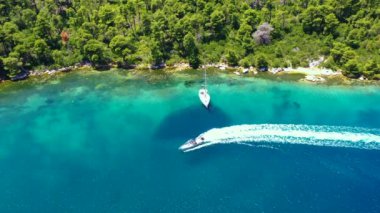 Yunanistan 'ın Limanaki Mplo Olyelos kentindeki güzel bir gölden sola dönen bir sürat teknesinin hava görüntüleri. Sürat teknesi sağdan geliyor ve sonra sola dönüyor. Ayrıca güzel mavi okyanusta bir yelkenli var. Hava aracı 4K