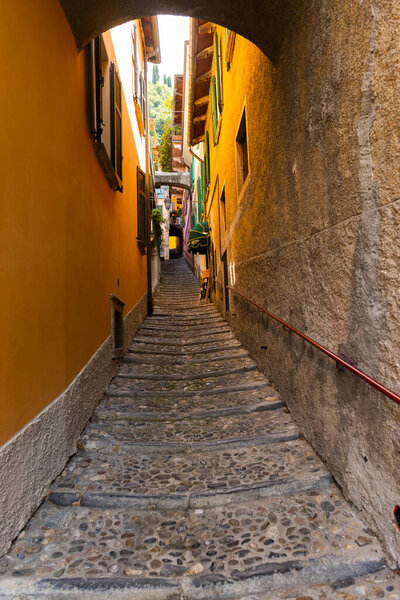Very narrow alley in Varenna, lake Como, Lombardy, Italy. Narrow alley between the residential buildings in the town of Varenna by the Como lake, Lombardy, Italy. Just a little sun comes down in the ally. Alley is very old and rustic